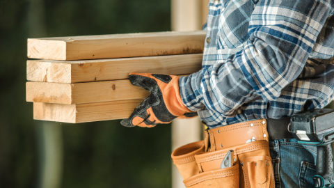 Person wearing construction apparel and gloves holding dimensional lumber